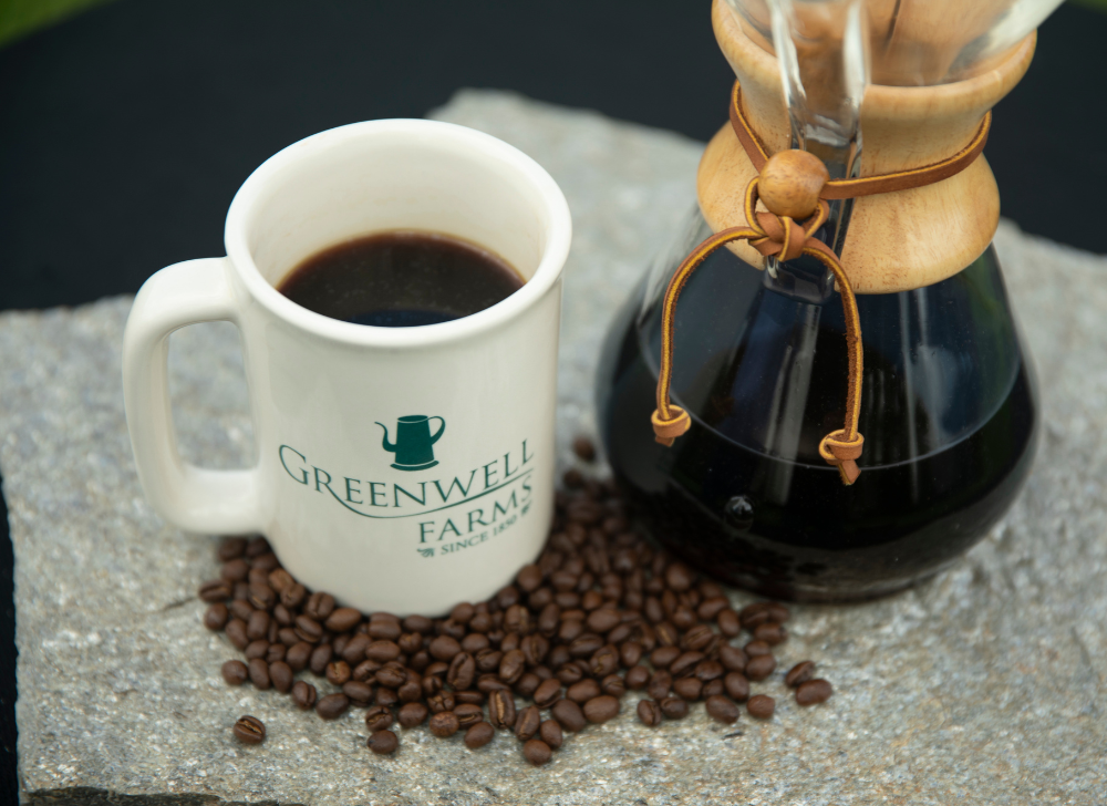 A cup of Greenwell Farms coffee beside a glass Chemex coffee maker